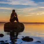 hübsche junge frau macht yoga auf einem Stein im Wasser See Meer im Sonnenuntergang Abendrot
