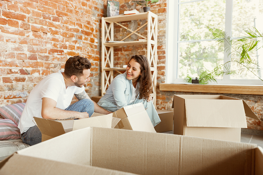 Young Couple Moved To A New House Or Apartment. Unpacking Cardbo